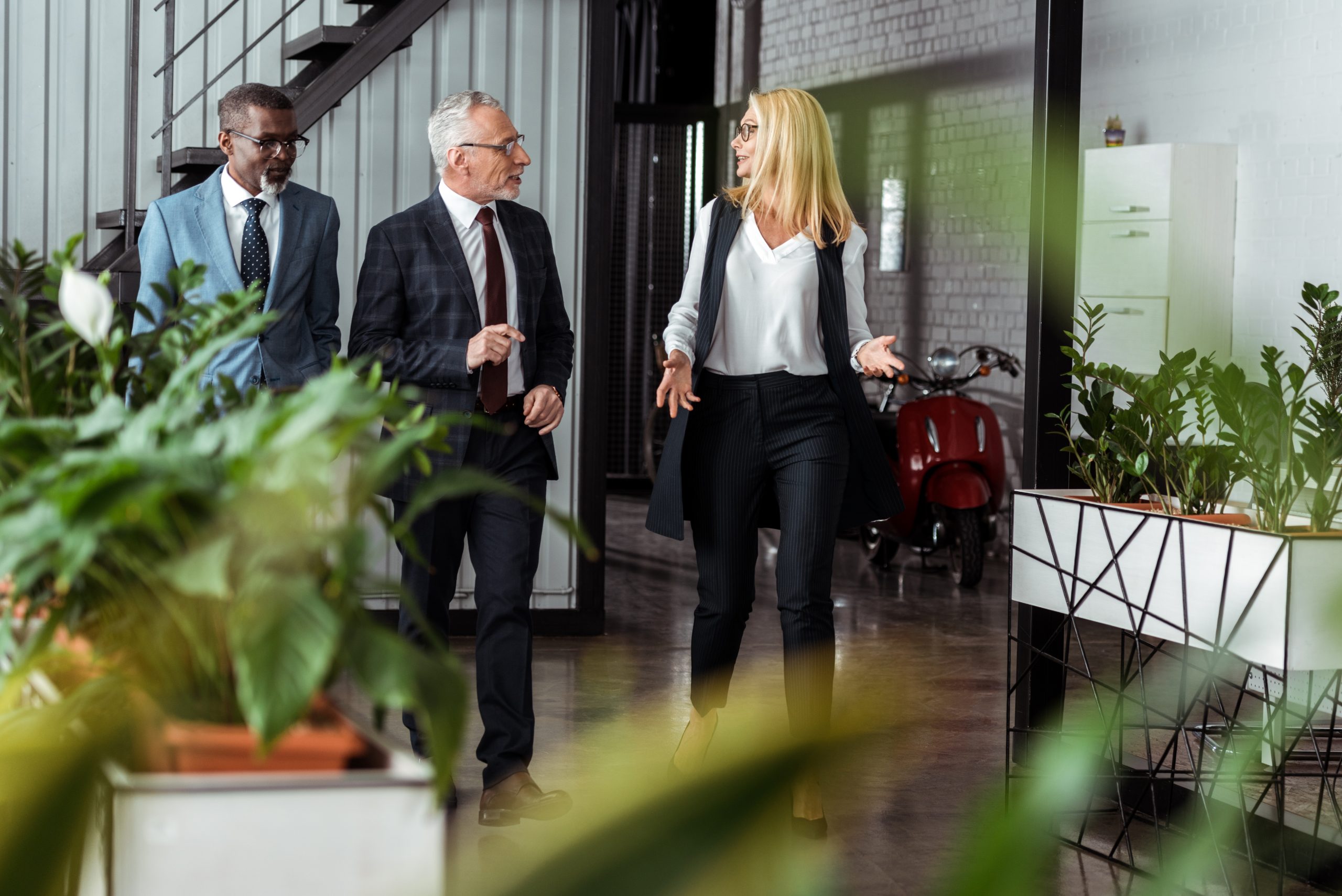 Selective focus of businesswoman gesturing while walking with partners in office.